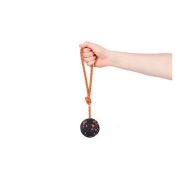 Mano sujetando la cuerda del juguete para perro Non-stop Dog ball on rope, mostrando la pelota con textura naranja y negra.